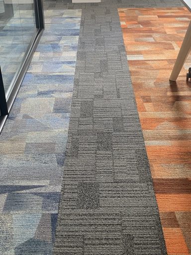 Carpet Tile Detail Installation Commercial flooring transition featuring carpet tiles, entrance matting and wood-effect LVT flooring within a modern office environment.